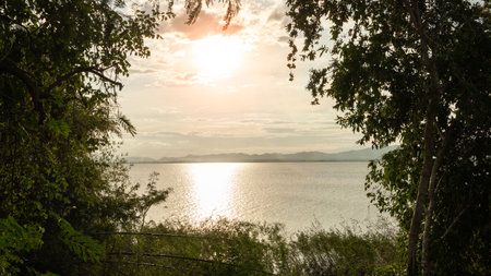 Location photos A large pool of clear water reflects the evening sunlight. obscured by green trees The sky is cloudy in the background. Looking far away, you can see mountains andの写真素材