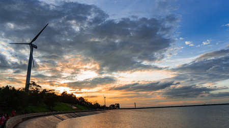 Image of the sun setting at the reservoir area. Nearby there are two wind turbines for generating...