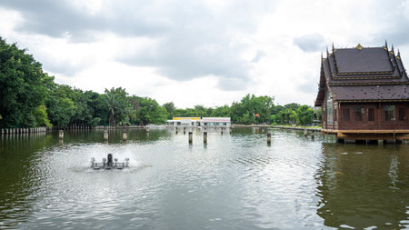 large pond picture There is one working wastewater treatment turbine. On the right is a Thai style pavilion. On the left is a garden. There are shady trees.の写真素材