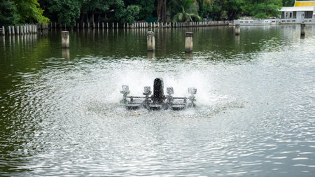 Picture of a working wastewater treatment turbine. There are 4 propellers that are rotating and hitting the water. Behind the working wastewater treatment turbine are 5 piers.の写真素材