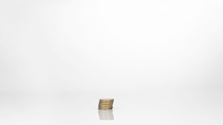 Coins are arranged in high and low shelves, mixed together. There is a reflection on the floor. Shows the value of money in today's economy. The background of the picture is white.の写真素材
