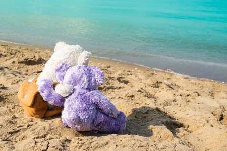 Couple teddy bear hugging each other on sand beach at coast with blue sea. card or poster for sweet love valentine day,broken heart, tourism vacation tropical travel summer in holiday concept.の写真素材