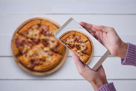 Hand woman with sweater photography pizza with smartphone. fast food and technology concept.の写真素材