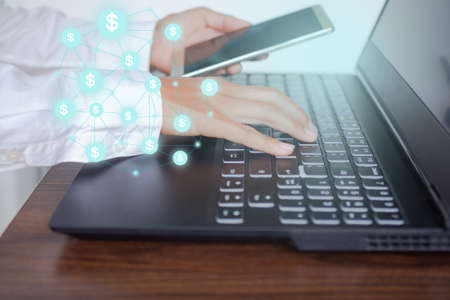 Staff woman typing keyboard computer laptop and holding smartphone with icon dollar symbols and lind network. planing earn financial and saving money future for 2022 new year. business and investment.の写真素材