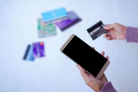 Hand woman holding smartphone mock up and credit card with book bank and credit card blured. for...