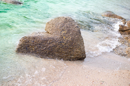 Stone heart shape nature authentic on sand beach and soft wave blue sea at coast. romantic love valentine days, broken heart or tourist travel summer in holidays.の写真素材