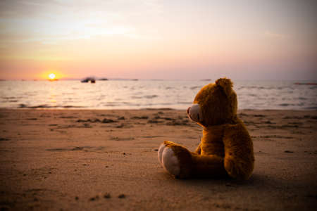 Single Teddy Bear on Sand Beach at Coast of Water Sea Shore Nature Sunset Background. Vintage with free space. Plush Toy symbols Lonely, Broken Heart, Lost Child,International Missing Children's Day.の写真素材