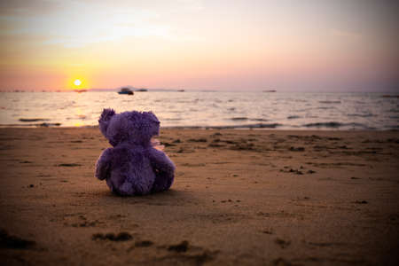 Single Teddy Bear on Sand Beach at Coast of Water Sea Shore Nature Sunset Background. Vintage with free space. Plush Toy symbols Lonely, Broken Heart, Lost Child,International Missing Children's Day.の写真素材