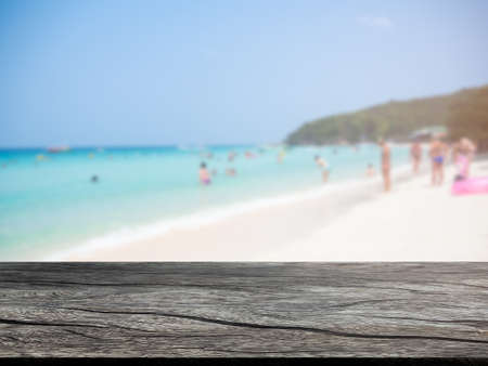 Wood perspective on people on sand beach at coats sea with empty table on blur image of sea and...