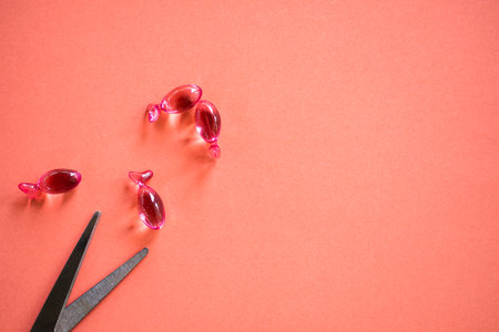 Gelatinous capsules vitamin E for face and scissors on red paper background. moisture oil to the skin, cosmetic for smooth. beauty and healthcare concept.の写真素材
