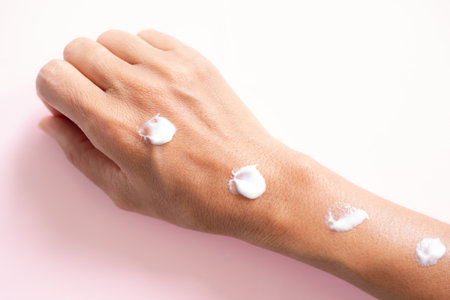 Flat lay hand woman apply cream lotion on pink paper. for sunscreen protection and moisture to the...