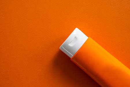 Sun block or sun screen tube on orange paper.cream or lotion cosmetics for woman on a day in the strong sunlight. for protect against UV A, UV B rays. tourist travel summer in holidays concept.の写真素材