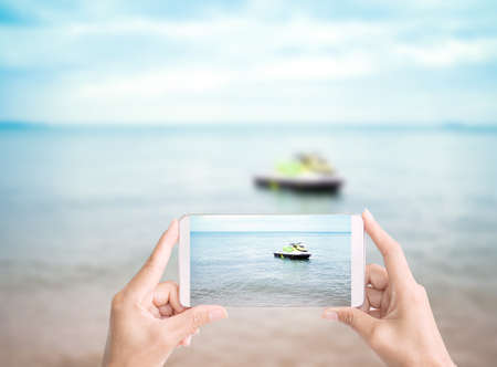 Hand holding Mobile photographer sea and speedboat at coast on blured blue ocean and blue sky in...