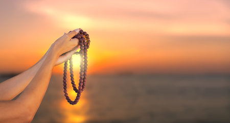 Hand woman holding rosary on blur image of sea and sky with sunset. female christian catholic religious faith praying.  religion Ramadan.の写真素材