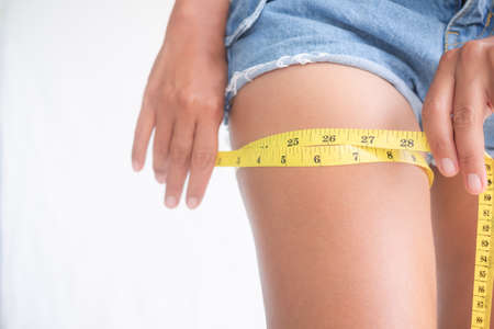 Woman with jean woman measuring her leg. slim fit body and authentic skin tan lady.control weight and diet for beautiful and good health concept.の写真素材