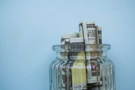 Cash bank 100 dollar in glass jar on blue background. close up saving money banknote for future. plan investment income for 2023 new year. business and finance concept.の写真素材