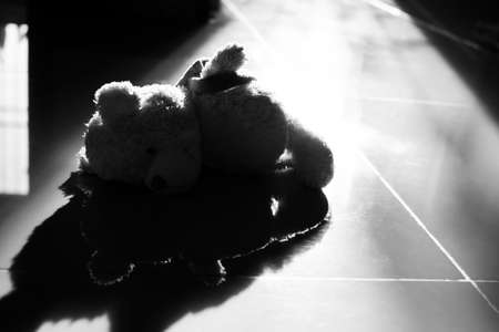 Alone teddy bear sleep on floor with overlight. black and white. cute toy doll in room with free  space. card or poster for lonely, sad, broken heart or international missing children's day concept.の写真素材