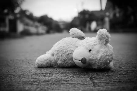 Teddy bear sleep on middle road with over light day and blur home. poster card for broken heart couple, sad, lonely, international missing Children, strong, gloomy day. alone unwanted cute doll lots.の写真素材