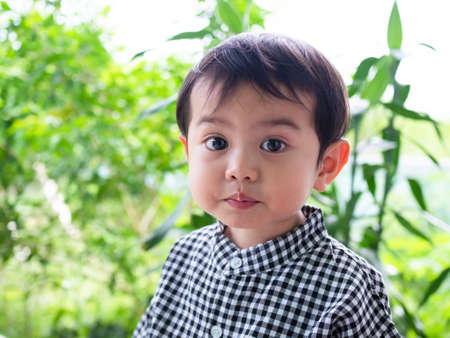 Portrait young boy 2 year old child with snack on cheek and green blur nature background. cute...