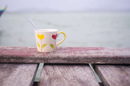 Coffee cup on wooden table with blur river water sea background.の写真素材
