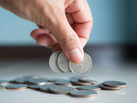 Stack coin.closeup finger woman holding money with blur pile cash on blue background.bank currency Thai. plan income investment growth and saving for 2023 new year.business or treasury finance conceptの写真素材