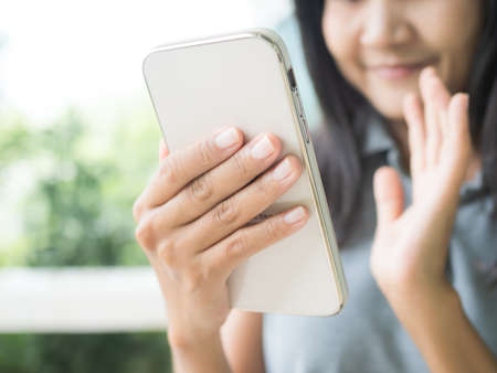 Woman video call mobile to friend she waving at home. people happy fun with technology communication digital hi speed internet chat online on camera smartphone with excited. business and lifestyle.の写真素材