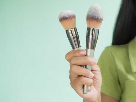 Hand Woman Holding Make Up brush Close Up on Green Cement Wall Background,Accessories Makeup Profeshional Costmetic,Blush brush Face Beautiful Products,Free Space for Presentation.の写真素材