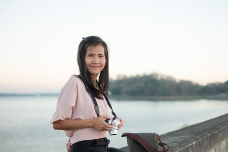 Portrait Alone Woman happy smile and holding Camera photography on blur river background.Tourist vacation Nature Tropical Travel Summer in Holidays concept. Authentic Slim fit, Black Hair and Skin Tanの写真素材
