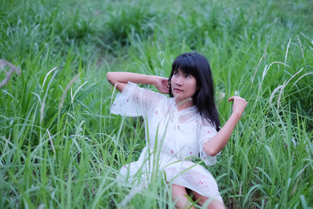 Portrait Alone Woman with white dress sitting on meadow for Rest at park. Authentic Slim fit, Black Hair and Skin Tan Asian Thailand.の写真素材
