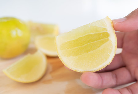 Finger holding Lemon Slice on wooden cutting board with white background,Yellow Lime Citron Raw Food Orgarnic Nature Tropical Fruits,Cooking Juice Drink in Kitchen,Hight Vitamin C for Diet Health.の写真素材