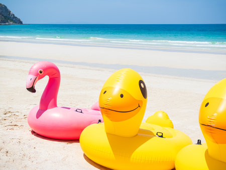 Ring Swim Inflatable Float on Sand Beach at Coast with blur Blue Sea and Sky Background, Pool Circle Yellow Rubber, Summer Tropical Tube,Pink Duck Flamingo Mattress on Water, Lifebuoy Lifesaver.の写真素材