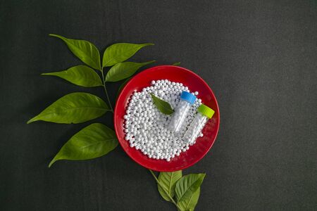 Top view of red plate filled with white sugar pills. Homeopathic medicine grains scattered on a red plate with green leaf on the black surfaceの写真素材