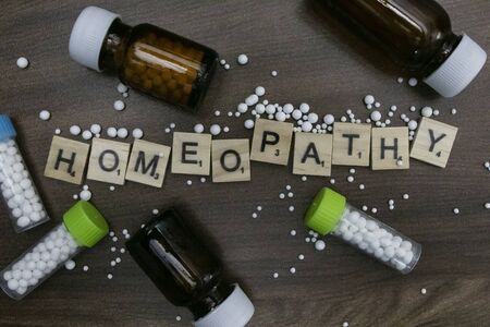 A homeopathy concept - Scattered pills with homeopathy substance bottles and text Homeopathy on...