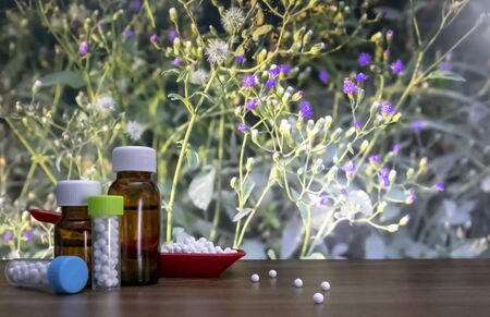 Homeopathic pills in red spoon and bottle of liquid and globules substance with spread white sugarballs on wood surface with wild flower backgroundの写真素材