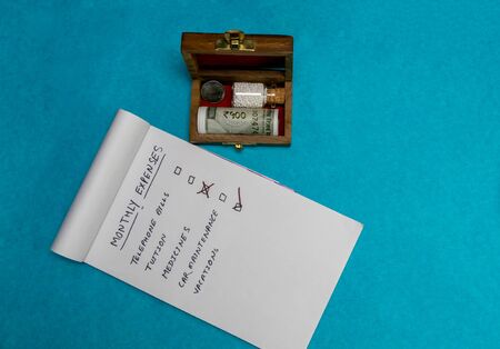 Glass Bottle of homeopathic medicine with coin and money in old wooden box with notepad on blue background, Money saving concept with homeopathyの写真素材