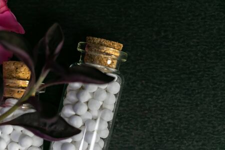 Natural medicine concept - Close up of homeopathic medicines bottles consisting of white sugar ball and fresh flower on dark backgroundの写真素材