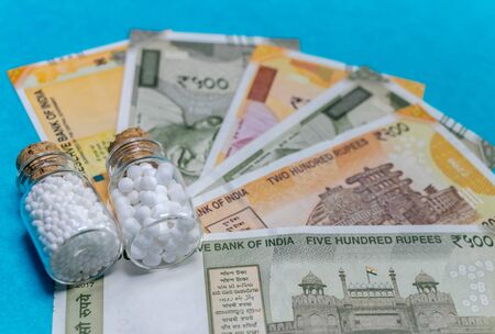 Homeopathy pills in vintage bottles with Indian currency on blue background - saving money with...