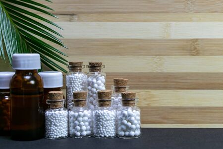 Medicine glass bottles consisting homeopathic substance with green leaf on wood and dark background....