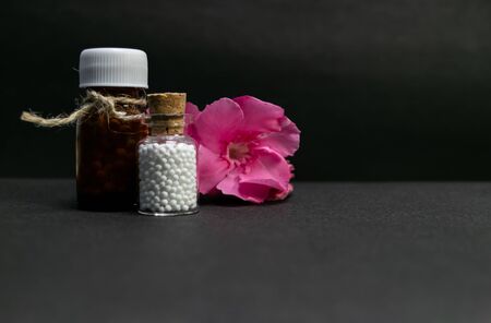 Natural Homeopathy - Close view of Homeopathic medicine bottles with pink flower buds on dark...