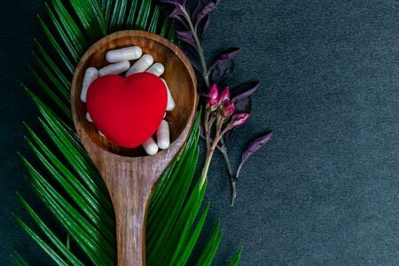 Red heart with Herbal medicines on wooden spoon and green leaf with wild pink flower on dark background. Herbal and natural medicine conceptの写真素材