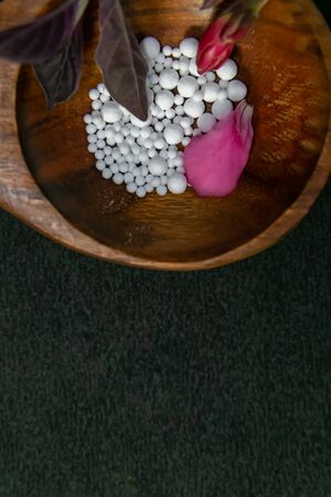 Scattered Homeopathic pills with pink flower petals in wood spoon on dark background. Natural medicine conceptの写真素材