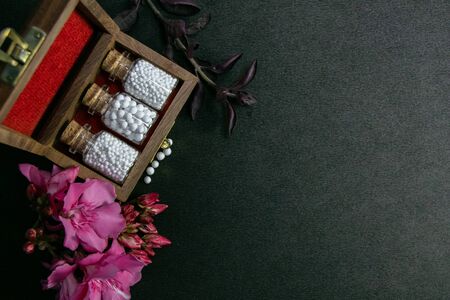Top view of homeopathic pills bottles with cork in wooden classic box and pink flowers on dark...