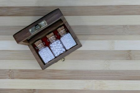 Top view of wooden box with homeopathic medicine glass bottles on wood background