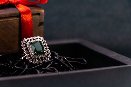 Anniversary gift concept. Close-up of Emerald ring in black box and wooden gift box with red ribbon...