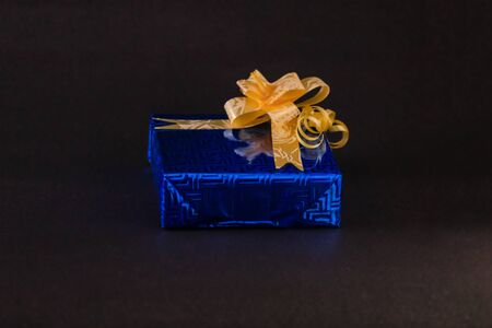 Blue gift box with golden ribbon bow on a dark contrast backgroundの写真素材