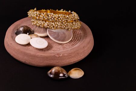 Traditional gift concept. Traditional Golden pearl bangle set with different seashells spreaded on black backgroundの写真素材