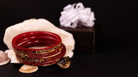 Beautiful red bangles on stone with seashells and brown lether box dcorated with white ribbon on black background. gift conceptの写真素材