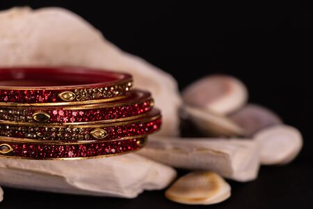 Traditional jewellery concept. Close-up of Beautiful red bangles on stone with spreaded seashells on...