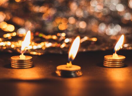 Three burning candles on pile of coins and bokeh in ht ebackground in Deepawali conceptの写真素材