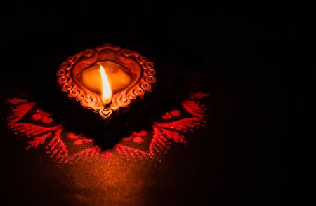 Beautiful single terracotta lamp glowing in the dark on a rangoli design with copy spaceの写真素材